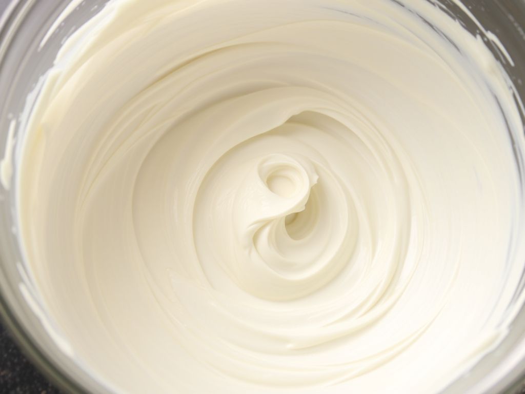 A close-up photograph of a clear glass bowl filled with smooth, creamy white oat cream, featuring a swirling texture and some splatters on the sides, suggesting it was just mixed